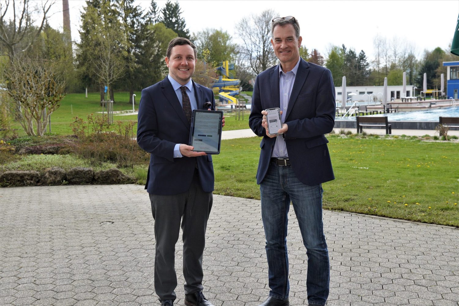der erste Bürgermeister Hans-Peter Dangschat und der Werkleiter zeigen stolz ein Tablet und ein Handy, auf dem der neue onlineshop der Stadtwerke zu sehen ist